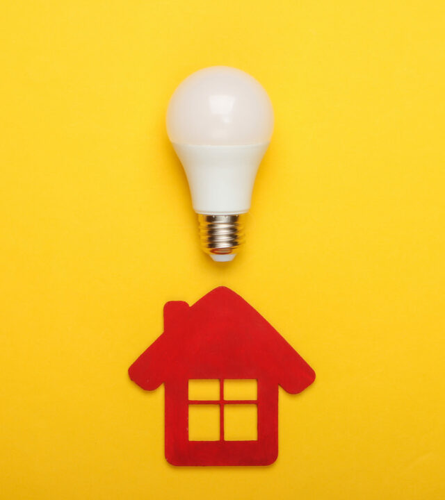 Energy saving concept. House figurine and energy-saving light bulb on yellow background. Top view